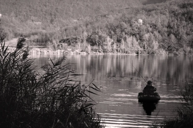 Fototapeta na ścianę w sepii przedstawiająca wędkarza na pontonie łowiącego ryby na tle lasu i jeziora