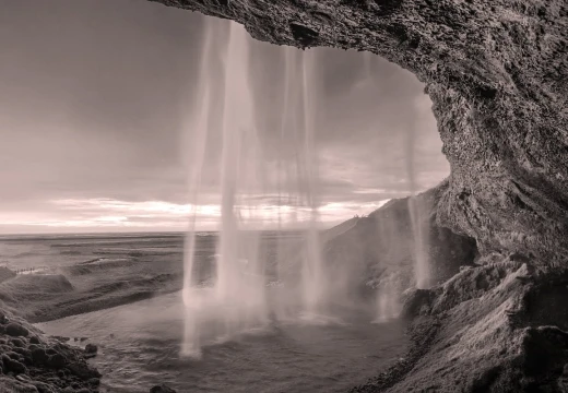 Fototapeta na ścianę z nadrukiem wodospadu Seljalandsfoss w Islandii w skali sepii, widocznego z wnętrza jaskini