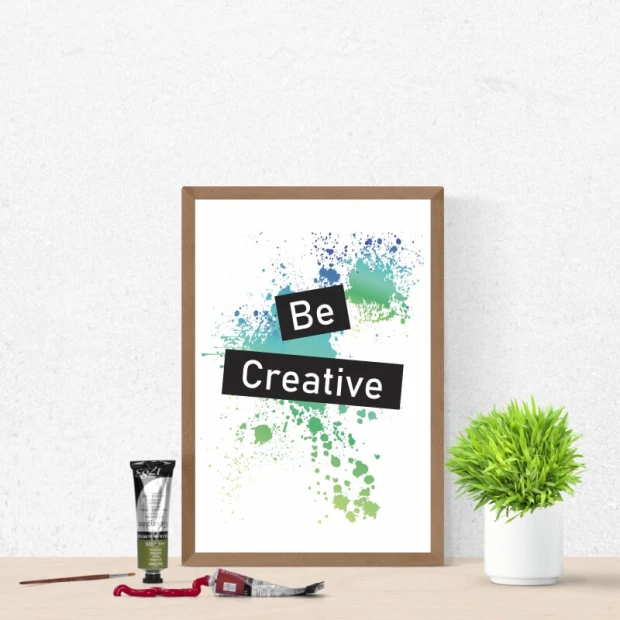 Plakat motywacyjny z napisem Be Creative na tle kolorowych plam farby, oprawiony w brązową ramę
