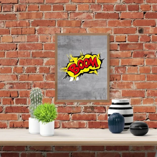 Plakat w drewnianej ramie z komiksowym napisem BOOM na szarym tle, zaprezentowany we wnętrzu