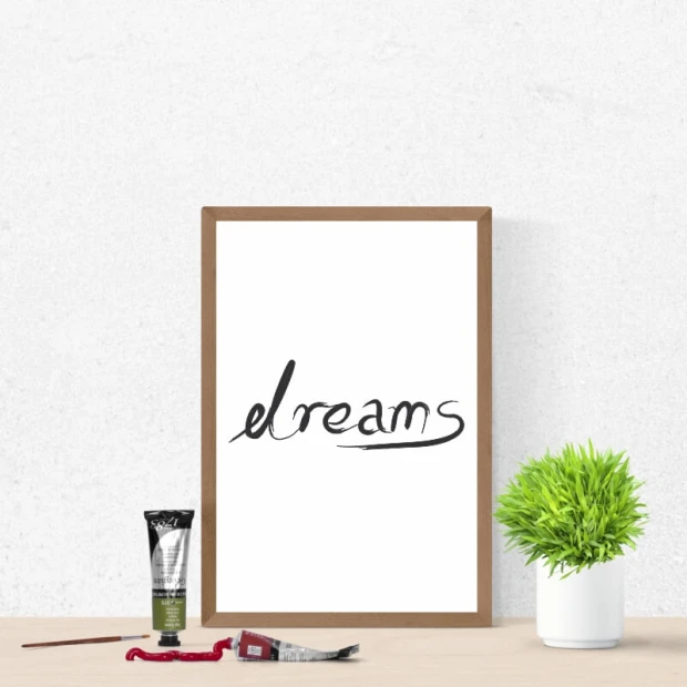 Plakat z czarnym, odręcznym napisem dreams na białym tle, oprawiony w jasnobrązową ramę