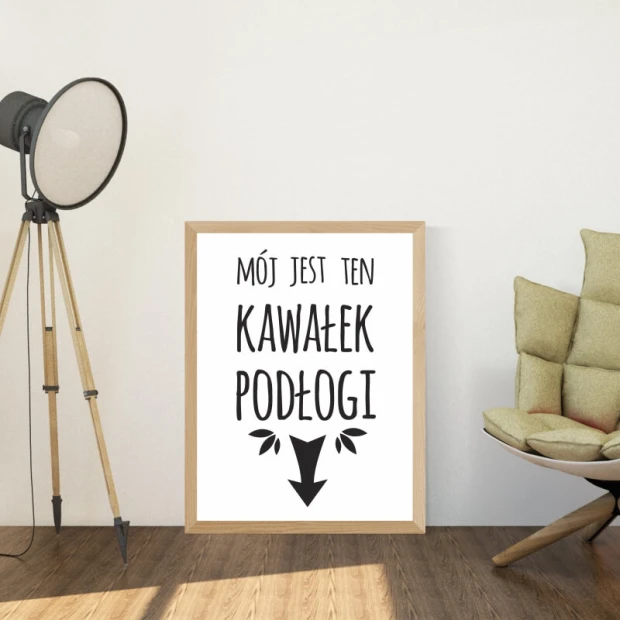 Plakat z czarnym napisem Mój jest ten kawałek podłogi i strzałką, oprawiony w jasną drewnianą ramę