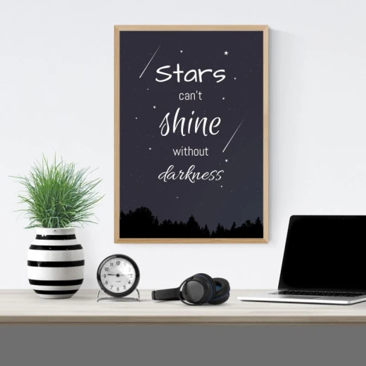 Plakat w jasnobrązowej ramie z angielskim cytatem o gwiazdach na tle nocnego nieba i sylwetek drzew