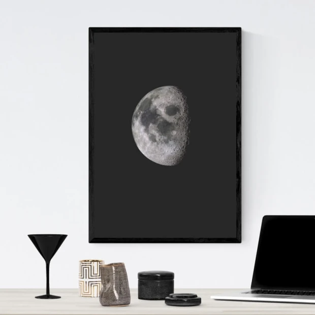 Plakat z nadrukiem księżyca w fazie pierwszej kwadry na ciemnym tle, oprawiony w czarną ramę we wnętrzu