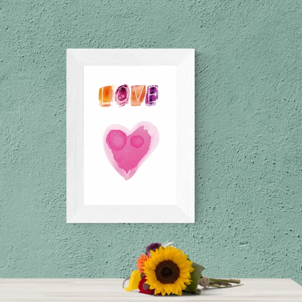 Plakat z kolorowym napisem Love oraz różowym sercem, zaprezentowany w białej ramie na ścianie