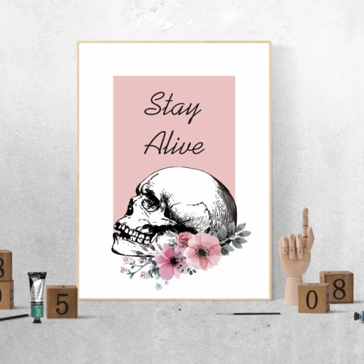 Plakat w jasnej ramie z motywem ludzkiej czaszki, różowych kwiatów oraz napisem Stay Alive na różowym tle