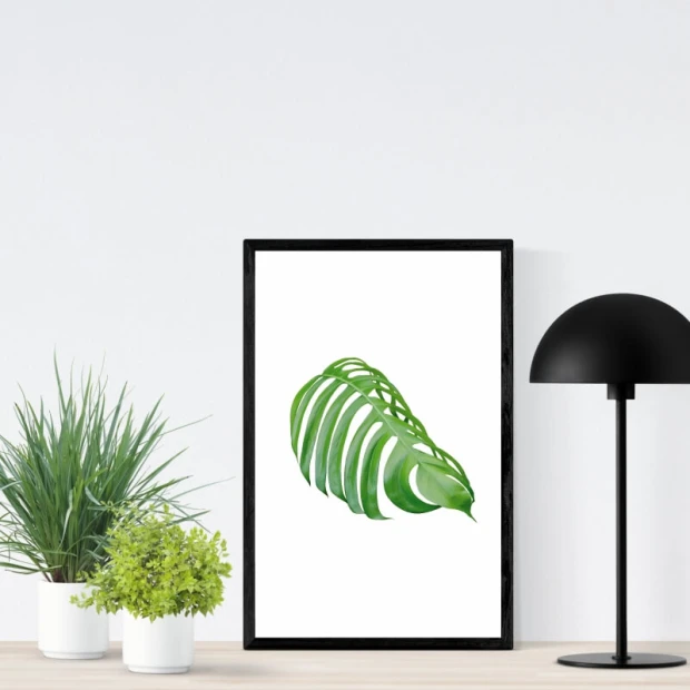 Plakat z nadrukiem zielonego liścia monstery w czarnej ramie zaprezentowany we wnętrzu