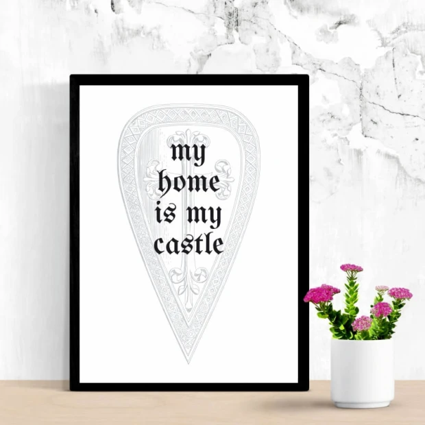 Plakat w czarnej ramie z angielskim napisem My home is my castle wpisanym w grafikę tarczy rycerskiej