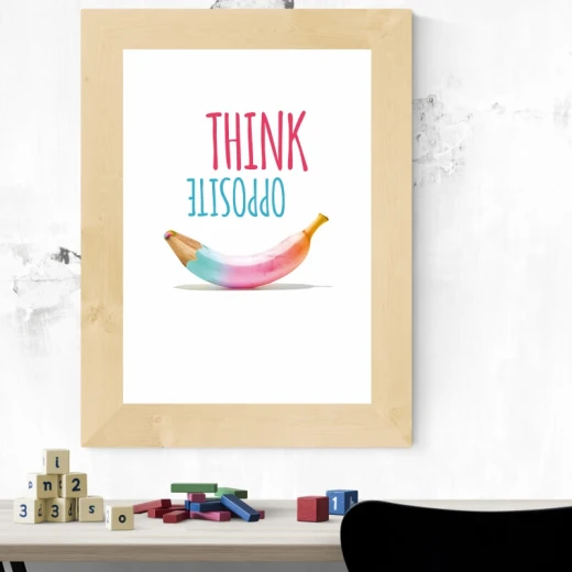 Plakat motywacyjny z napisem Think opposite i grafiką banana w jasnej, drewnianej ramie zawieszony we wnętrzu