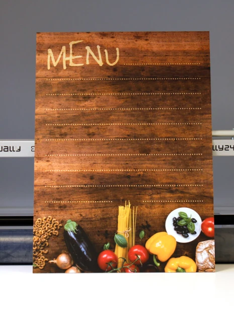 Tablica kredowa z nadrukiem imitującym drewno, napisem MENU i grafiką warzyw w ujęciu na maszynie produkcyjnej