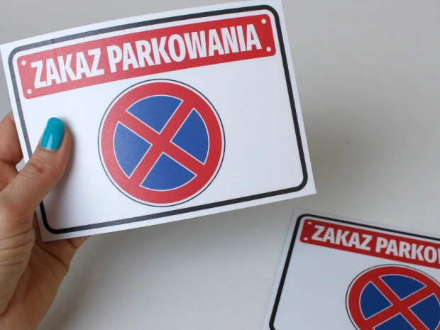 Naklejka parkingowa Zakaz parkowania trzymana w dłoni, z czerwonym napisem i niebiesko-czerwonym znakiem zakazu