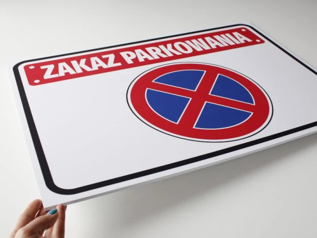 Tabliczka Zakaz parkowania T039 - Wzór graficzny. Prostokątna tabliczka z czerwonym napisem i niebieskim symbolem