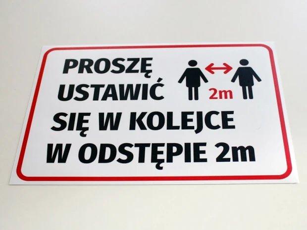Czerwono-czarna naklejka BHP o zachowaniu odstępu 2m naklejona na gładką powierzchnię, pokazana pod kątem