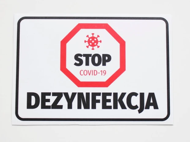 Naklejka BHP z czerwonym symbolem stop, wirusem i napisem DEZYNFEKCJA w czarnej ramce na białym tle