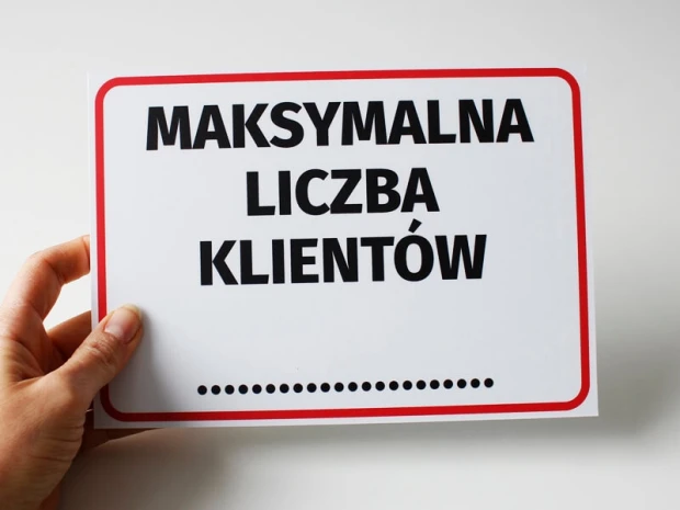 Tabliczka Maksymalna liczba klientów trzymana w dłoni, pokazująca rzeczywisty produkt i jego wielkość