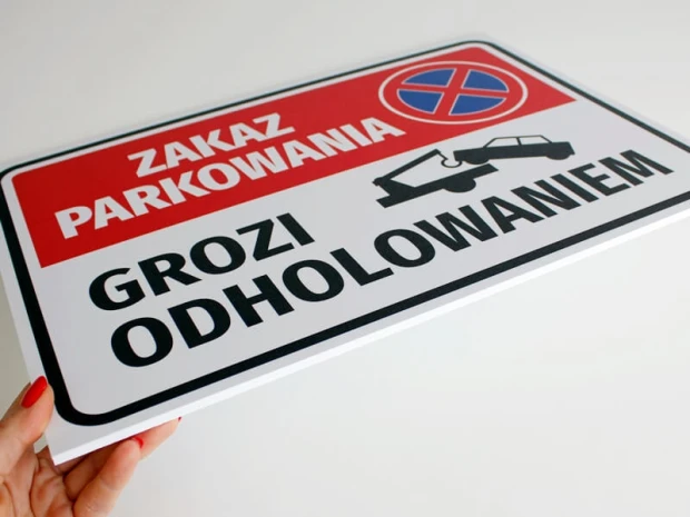 Tabliczka Zakaz parkowania grozi odholowaniem trzymana w dłoni, prezentująca zaokrąglone narożniki i grubość płyty