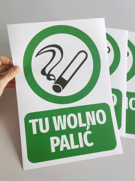 Zielona naklejka BHP TU WOLNO PALIĆ z piktogramem papierosa trzymana w dłoni jako gotowy produkt