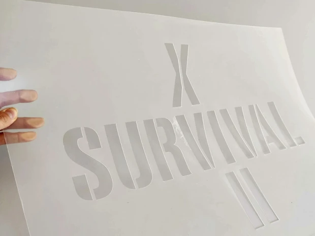 Prostokątny szablon malarski z wyciętym napisem SURVIVAL, prezentowany na zdjęciu fizycznego produktu