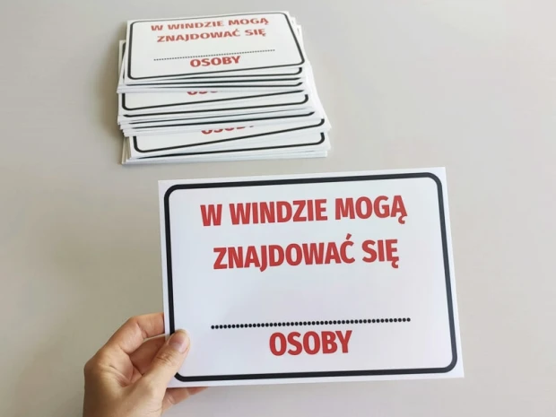 Naklejki BHP do windy z czerwonym napisem o limicie osób, pokazane jako stos gotowych produktów