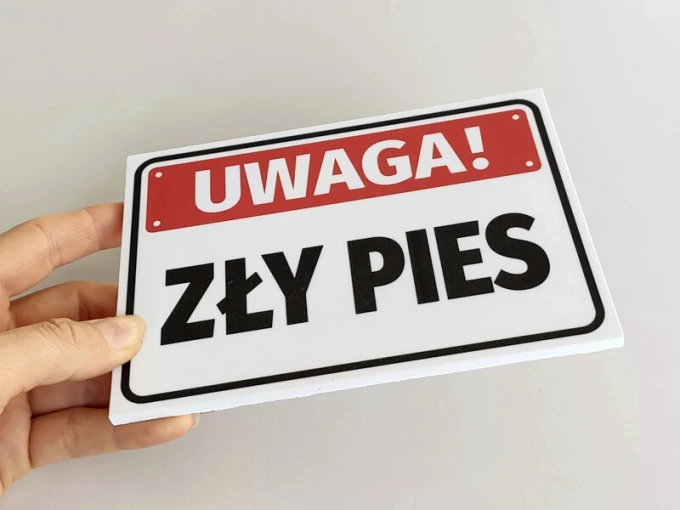 Tabliczka Uwaga, zły pies - Wzór graficzny. Prostokątna tabliczka z czerwonym tłem i dużymi czarnymi literami