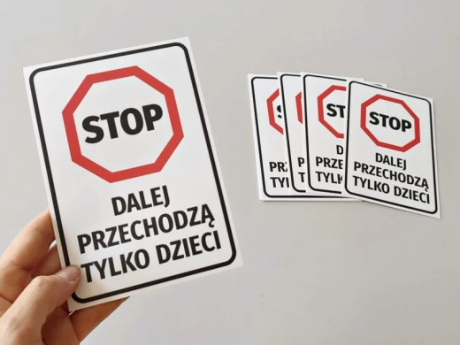 Naklejka BHP ze znakiem stop i napisem o przejściu dla dzieci, trzymana w dłoni na tle kilku sztuk produktu