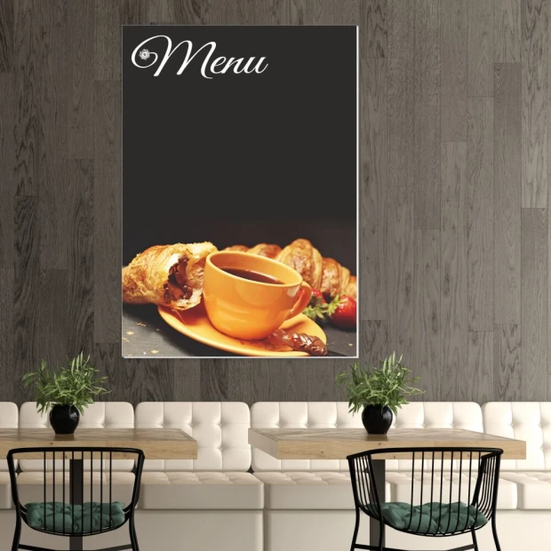 Tablica kredowa z nadrukiem napisu Menu oraz grafiki z filiżanką kawy i croissantami we wnętrzu lokalu