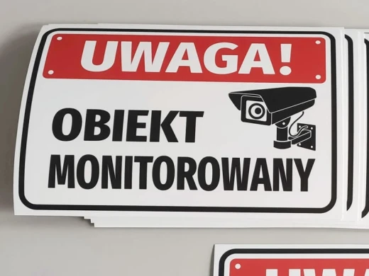 Naklejki BHP Uwaga obiekt monitorowany z czerwoną belką i czarną kamerą, ułożone w stos