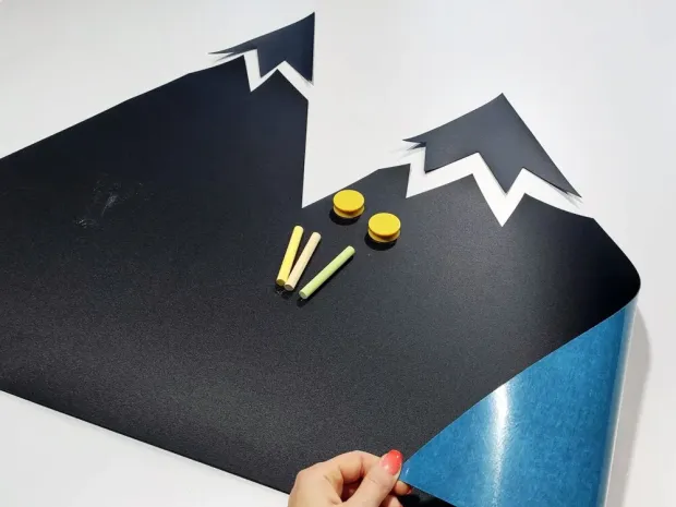 Tablica magnetyczna kredowa w kształcie gór w ujęciu pokazującym odklejanie warstwy ochronnej z kleju