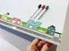 Tablica magnetyczna suchościeralna dla dzieci miasto 495 - Wzór graficzny. Na tablicy przedstawiono ulicę z domami, drzewami