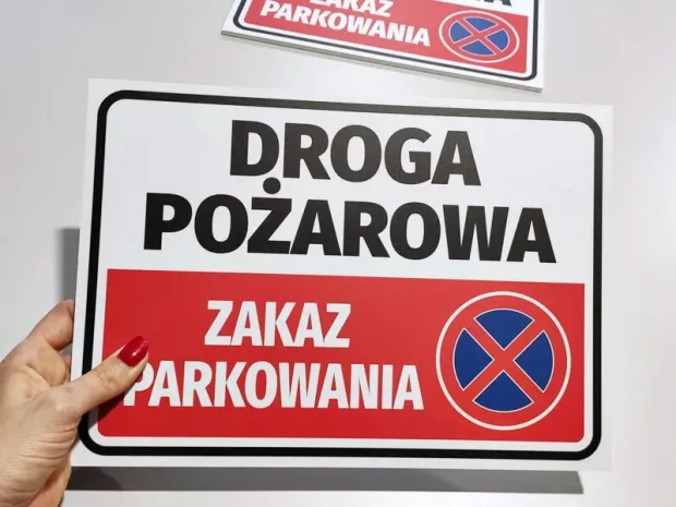 Tabliczka Droga pożarowa zakaz parkowania ze znakiem zakazu postoju, trzymana w dłoni jako prezentacja produktu