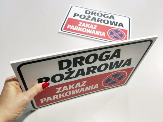 Tabliczka Droga pożarowa zakaz parkowania trzymana w dłoni w ujęciu pokazującym grubość sztywnej płyty