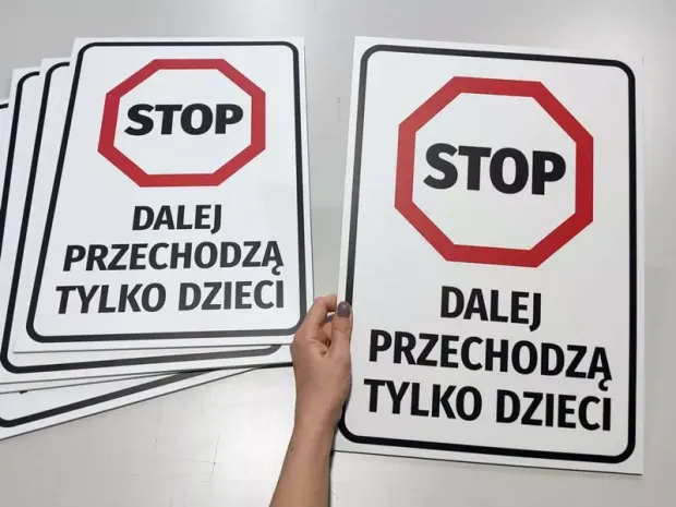 Tabliczka BHP Stop dalej przechodzą tylko dzieci trzymana w dłoni na tle stosu gotowych tabliczek