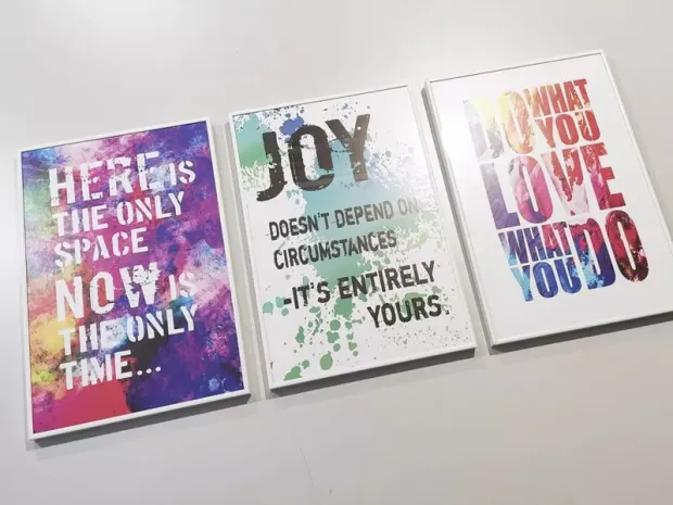 Trzy plakaty w białych aluminiowych ramach z motywacyjnymi napisami po angielsku na kolorowym tle