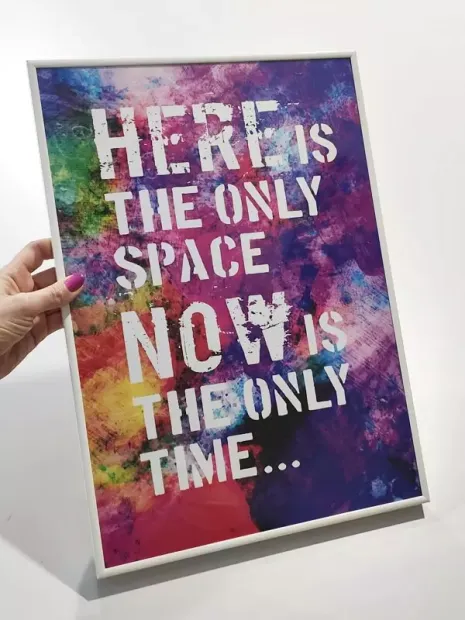 Plakat w białej ramie z angielskim napisem motywacyjnym na kolorowym tle trzymany w dłoni
