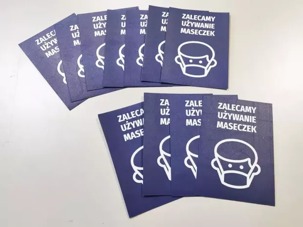 Niebieskie naklejki BHP z napisem Zalecamy używanie maseczek i piktogramem, pokazane jako zestaw kilku sztuk