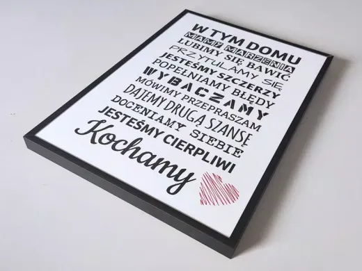 Plakat z napisem W tym domu i różowym sercem w czarnej ramie, leżący płasko i pokazany pod kątem