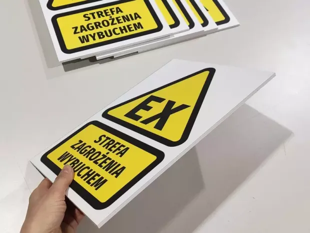 Tabliczka BHP Strefa zagrożenia wybuchem z żółtym znakiem EX trzymana w dłoni, pokazująca grubość płyty PCV