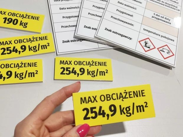 Suchościeralne tabliczki z nadrukiem obciążenia regałów trzymane w dłoni dla pokazania ich rzeczywistego rozmiaru