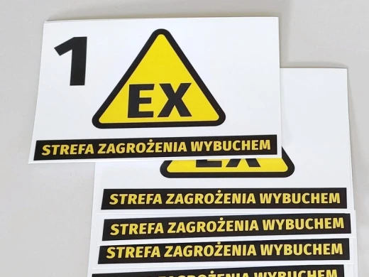 Fizyczne naklejki BHP ostrzegające przed wybuchem, ułożone w stos pokazujący grubość i formę arkusza