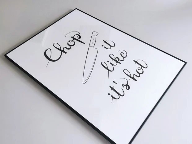 Plakat z napisem Chop it like it\'s hot w czarnej ramie leżący na płaskiej powierzchni, pokazany pod kątem