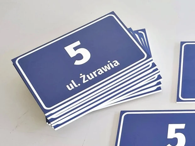Niebieska tabliczka adresowa z polem na numer domu i nazwę ulicy, pokazana w stosie gotowych produktów