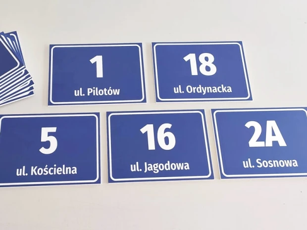 Niebieskie tabliczki adresowe z przykładowym numerem domu i nazwą ulicy, pokazane w zestawie kilku sztuk