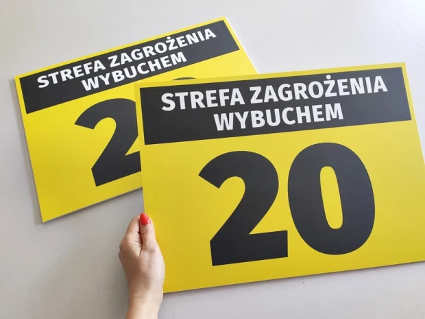 Dwie żółte tabliczki BHP z napisem STREFA ZAGROŻENIA WYBUCHEM 20, prezentowane w dłoni jako fizyczny produkt