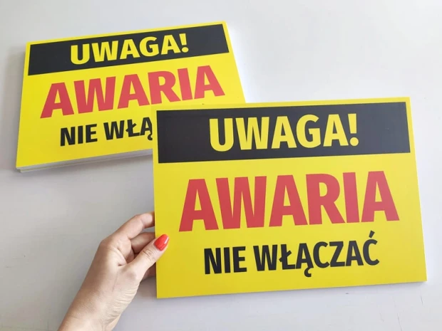 Żółta tabliczka ostrzegawcza Uwaga awaria, nie włączać trzymana w dłoni, pokazująca fizyczny produkt