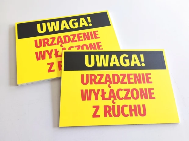 Dwie żółte tabliczki BHP z napisem UWAGA! URZĄDZENIE WYŁĄCZONE Z RUCHU, pokazujące grubość fizycznego produktu