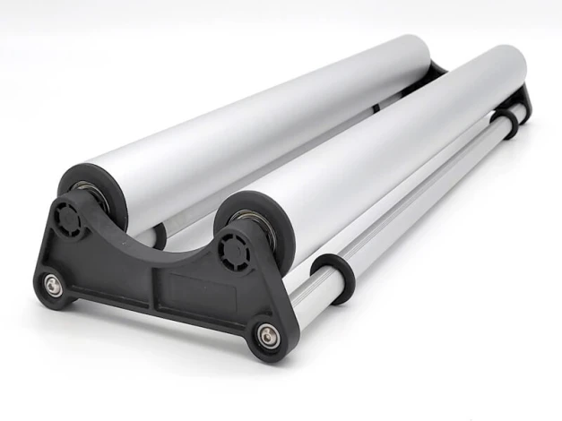 Rozwijarka do mediów reklamowych - Wzór graficzny. Dwa cylindryczne elementy w kolorze srebrnym na czarnej podstawie