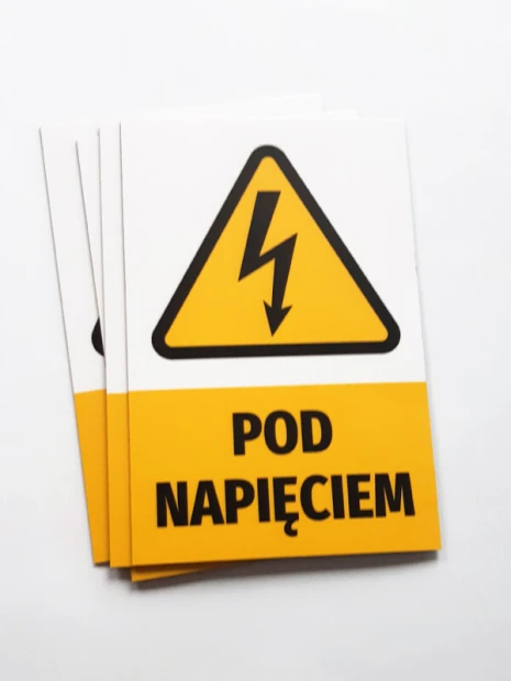 Prostokątne magnesy z przykładowym ostrzeżeniem POD NAPIĘCIEM, ułożone w lekki stos na białym tle