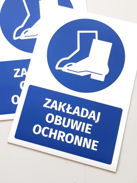Dwie niebieskie naklejki BHP nakazu Zakładaj obuwie ochronne w ujęciu pokazującym fizyczny produkt