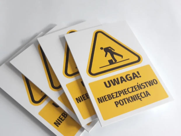 Tabliczka ostrzegawcza BHP z piktogramem Uwaga! Niebezpieczeństwo potknięcia - Wzór graficzny. Żółty trójkąt z czarnym