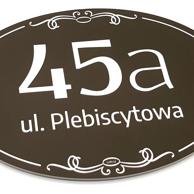 Brązowa owalna tabliczka adresowa w zbliżeniu pokazującym grubość płyty oraz matowe wykończenie nadruku